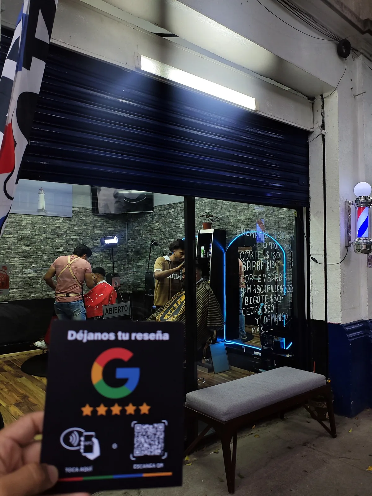 El letrero NFC en la mano, frente a Barba Dei abierta y con clientes.