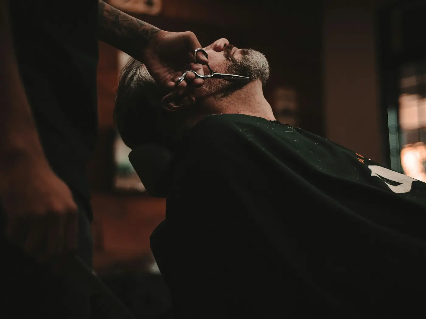 Barbero recortando la barba de un cliente en una barbería con luz cálida.