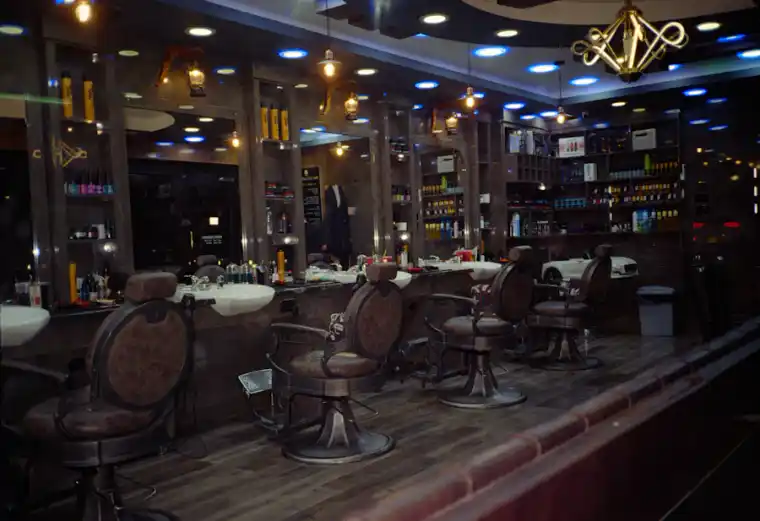 Interior de barbería con sillas y espejos, ambiente cálido.
